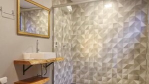 Um banheiro com vaso sanitário, pia com bancada de madeira, espelho com moldura dourada e chuveiro com parede de azulejos geométricos.