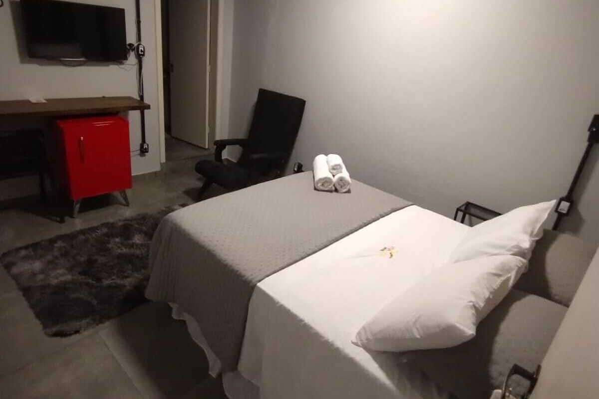 A hotel room with two beds, a desk with a TV, a red minibar, and a chair.