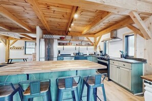 Una cocina con una isla central, taburetes de bar, vigas de madera en el techo y un ventanal.