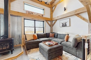 A cozy living room with a sectional sofa, a wooden ceiling, and a large window.