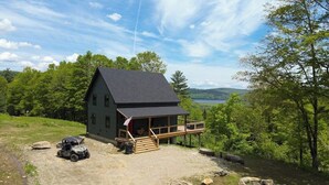 A cabin with a deck, surrounded by trees and a lake view.