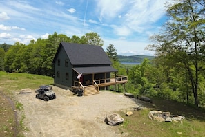A cabin with a deck, surrounded by trees and a lake view.