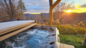 A hot tub with a wooden deck and a view of a mountainous landscape.