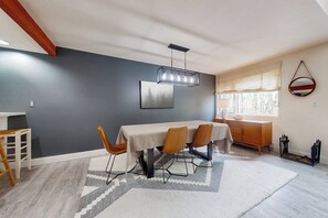 A dining area with a table, chairs, a hanging light fixture, and a window with curtains. - Cozy Townhome with Shared Pool, W/D & Wood-Burning Fireplace (Stratton)