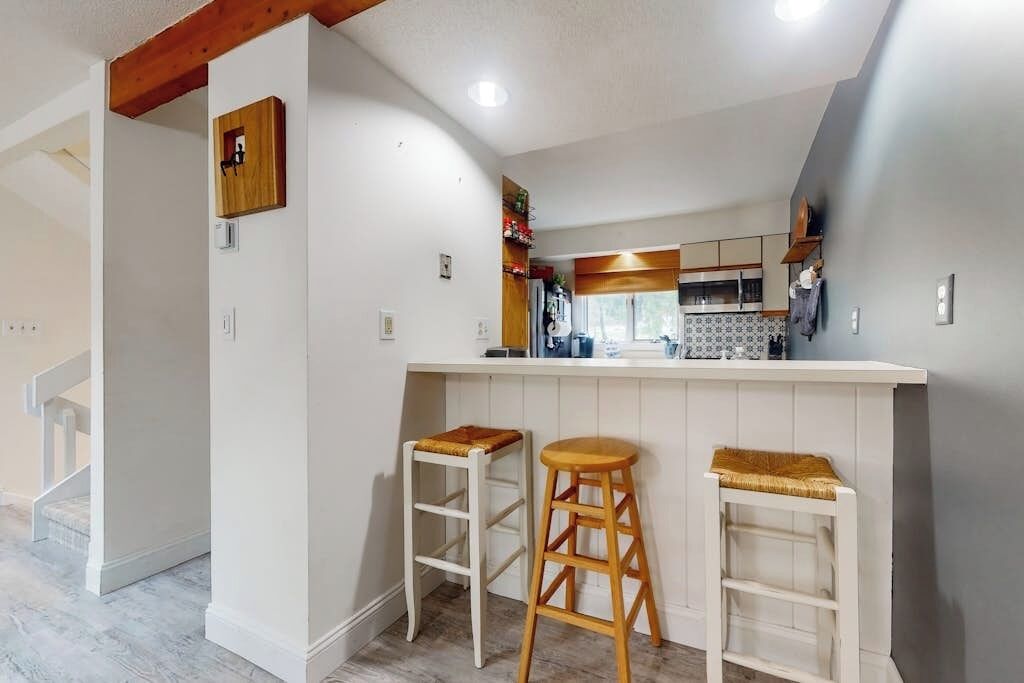 A kitchen with a white countertop, two wooden stools, and a wooden beam ceiling.