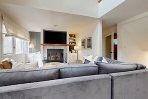 A living room with a fireplace, grey sofa, and a television. - Cozy Townhome with Shared Pool, W/D & Wood-Burning Fireplace (Stratton)