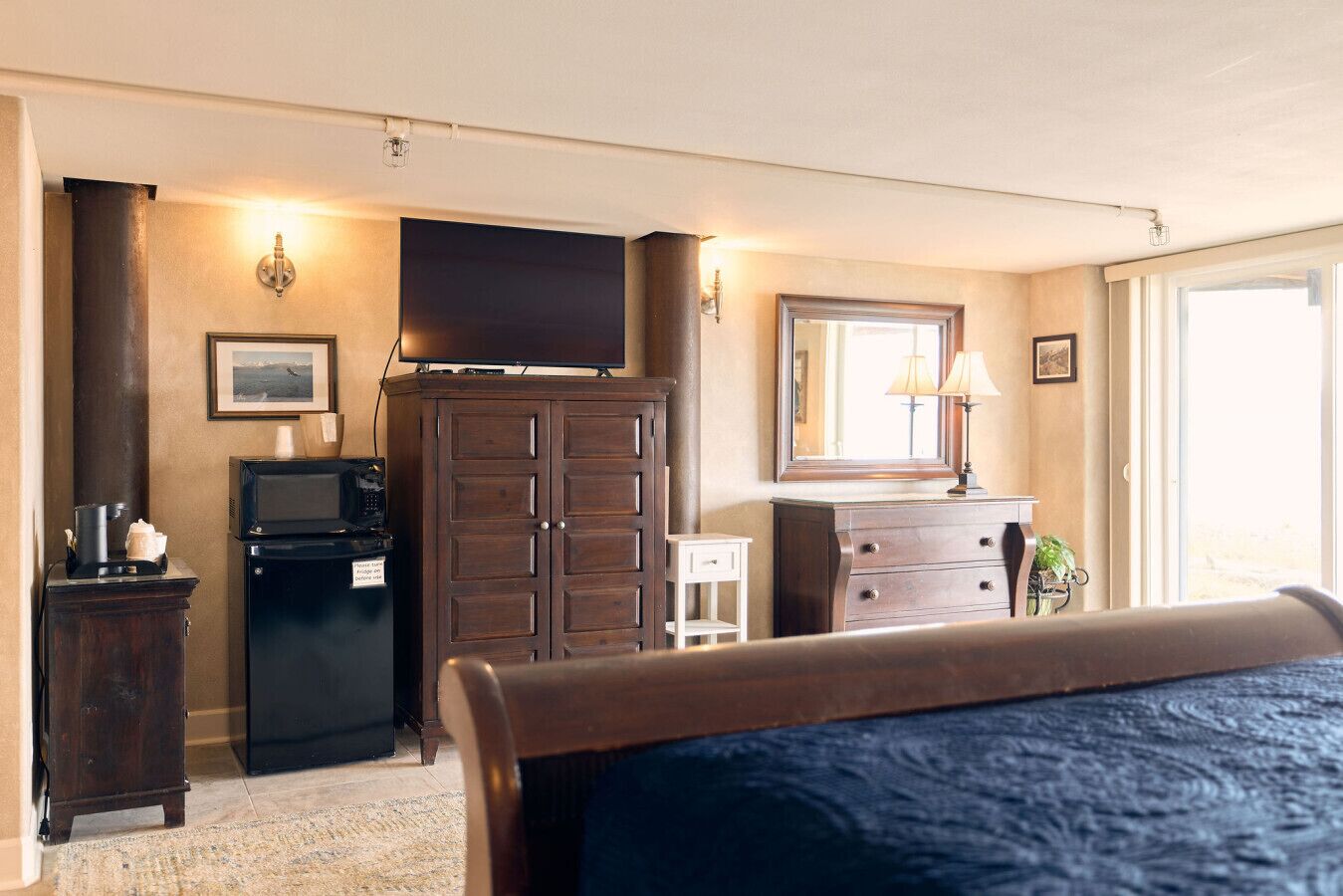 Un dormitorio con cama, televisión, armario, una mesita y espejo.