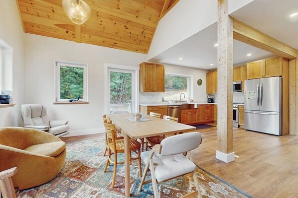 A spacious kitchen with wooden cabinets, a dining area with a table and chairs, and a large window providing a view of the outdoors. - Beautiful house w/ mountain view, balcony, grill, central a/c, close to skiing (Ludlow)