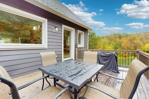 A deck with a table and chairs, a covered table, and a view of a forested landscape. - Beautiful house w/ mountain view, balcony, grill, central a/c, close to skiing (Ludlow)
