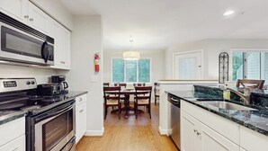 Une cuisine moderne équipée d’un four à micro-ondes, d’une cuisinière et d’un évier, ainsi que d’une table à manger en bois et d’un lustre.