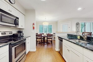 A modern kitchen with a microwave, stove, and sink, wooden dining table, and a chandelier. - Updated ground floor condo w/ patio, fireplace, ski locker, door to door shuttle (Stratton)