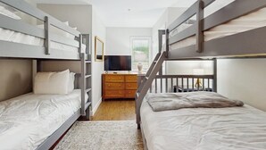 Une chambre avec des lits superposés, une commode, un téléviseur et une fenêtre avec des stores.
