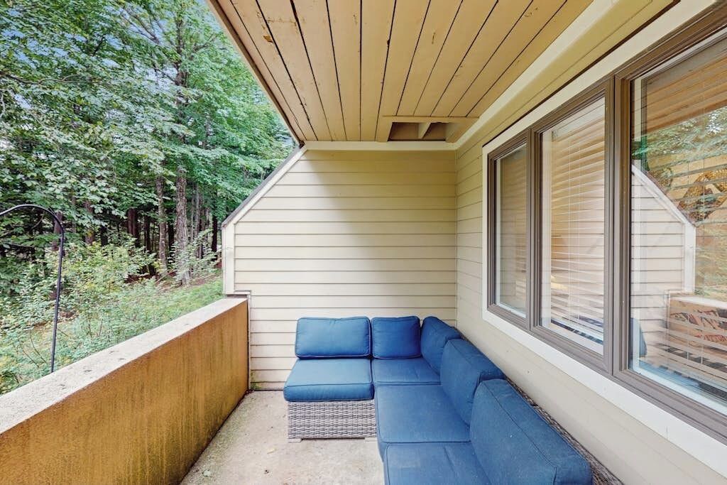 Un balcon abrité avec un canapé bleu, un plafond en bois et une vue sur les arbres.