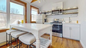 Eine Küche mit weißen Schränken, einer Mikrowelle, einem Backofen und einem Essbereich mit weißem Tisch und Barhocker.