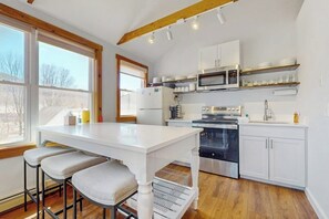 Eine Küche mit weißen Schränken, einer Mikrowelle, einem Backofen und einem Essbereich mit weißem Tisch und Barhocker.