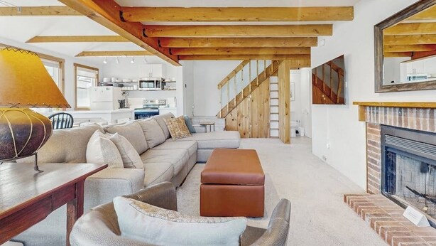 Ein modernes Wohnzimmer mit Ecksofa, Kamin, freiliegenden Holzbalken und einer Küche im Hintergrund.