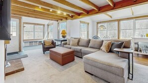 Ein geräumiger Wohnbereich mit einer großen Couch, Hocker und Holzbalken an der Decke.