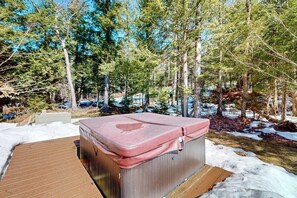 Un jacuzzi en un área boscosa con nieve en el suelo.