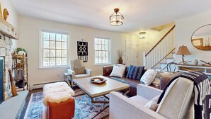 A living room with a fireplace, a sofa, a coffee table, and a staircase. - Delightful house w/ hot tub, wrap-around deck, ping-pong-pool table, fireplaces (Ludlow)
