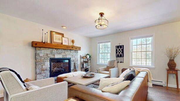 A living room with a stone fireplace, a sofa, a coffee table, and a television. - Delightful house w/ hot tub, wrap-around deck, ping-pong-pool table, fireplaces (Ludlow)