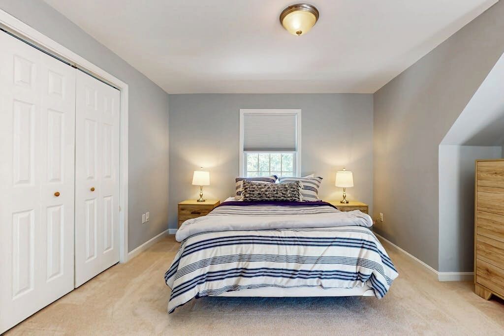 A bedroom with a bed, two bedside tables with lamps, a window, and a door.