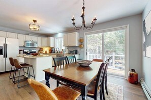 A modern kitchen with white cabinets, a dining table with chairs, a chandelier, and a large window.
