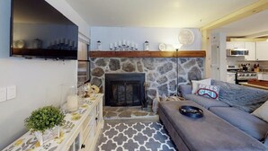 A living room with a stone fireplace, a flat-screen TV mounted on the wall, a sofa, and a patterned rug.