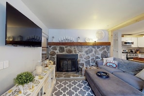A living room with a stone fireplace, a flat-screen TV mounted on the wall, a sofa, and a patterned rug. - Dog-friendly home w/ WiFi, private washer/dryer, and electric fireplaces (West Dover)