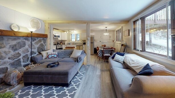 A modern living room with a stone accent wall, a grey sofa, a patterned rug, and a dining area with a table and chairs.
