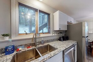 A kitchen with a stainless steel sink, a window with a view of a snowy deck, white cabinets, and a refrigerator. - Dog-friendly home w/ WiFi, private washer/dryer, and electric fireplaces (West Dover)
