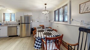 A modern kitchen with a stainless steel refrigerator, a dining table with checkered tablecloths, and wooden chairs.
