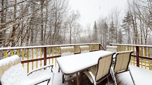 A snow-covered deck with a table and chairs, surrounded by trees.