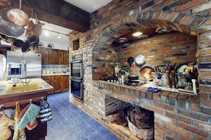 Eine Küche mit Kamin aus Backstein, hängenden Töpfen und einem Edelstahl-Kühlschrank.