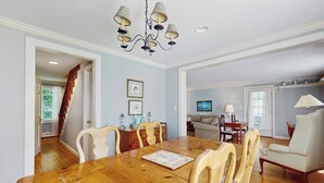 Ein Essbereich mit Holztisch und -stühlen, einer Chandelüster und Blick in einen angrenzenden Raum mit Sofa und Fernseher.