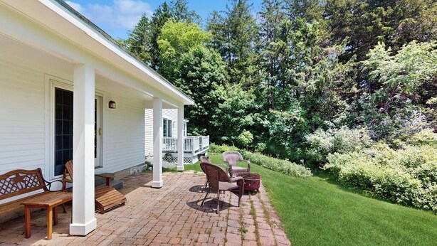 Eine überdachte Terrasse mit Backsteinpflasterung, Gartenmöbeln und einem üppigen grünen Rasen.