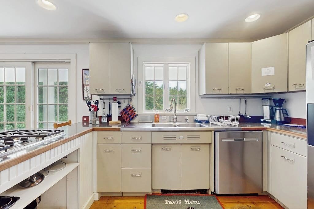 A kitchen with white cabinets, a sink, a dishwasher, and a window.