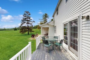 A house with a deck, a dining table with chairs, and a view of a green field. - Spacious village house, dog-friendly, patio, fireplace, a/c, air hockey, w/d (Manchester)