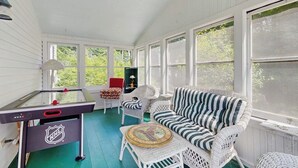 Ein Wintergarten mit Billardtisch, einer Couch und Korbstühlen.