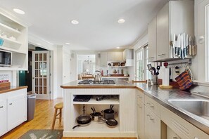 A modern kitchen with white cabinetry, a central island, and a variety of kitchen utensils. - Spacious village house, dog-friendly, patio, fireplace, a/c, air hockey, w/d (Manchester)