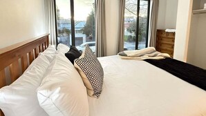 A hotel room with a bed, a wooden headboard, a dresser, and a view of the outside. - Stadium Gatehouse - Bookahome (Central City Christchurch)