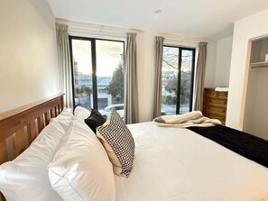 Ein Hotelzimmer mit Bett, Holz-Kopfstütze, Kommode und Blick nach draußen.