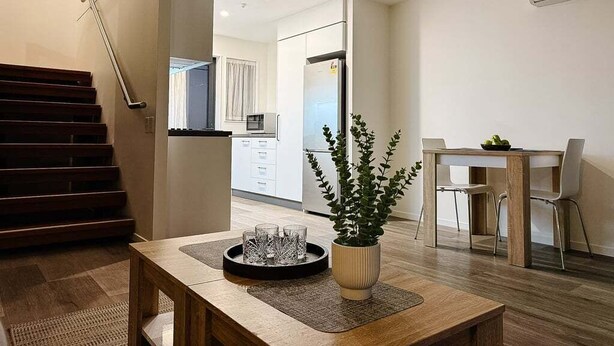 A modern living space with a dining area, kitchen, and staircase. - Stadium Gatehouse - Bookahome (Central City Christchurch)