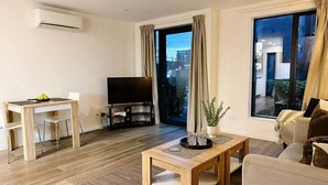 A modern living room with a sofa, a coffee table, a TV, and a dining area with chairs and a table. - Stadium Gatehouse - Bookahome (Central City Christchurch)