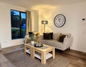 Ein Wohnzimmer mit einer Couch, einem Couchtisch, einer Uhr und einem Fenster mit Vorhängen.