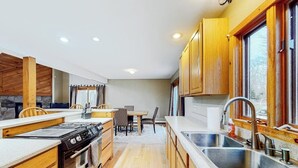 A compact kitchen with wooden cabinets, a stove, a sink, and a dining area with chairs. - Exquisite home with fireplace, balcony, fast WiFi, jetted tub & washer/dryer (West Dover)