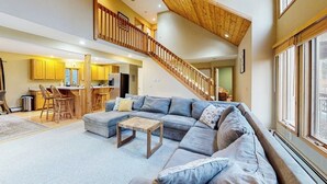 A spacious living area with a large sectional sofa, a wooden coffee table, and a staircase leading to an upper level. - Exquisite home with fireplace, balcony, fast WiFi, jetted tub & washer/dryer (West Dover)