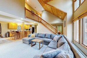 Ein geräumiger Wohnbereich mit einer großen Eckcouch, einem Holztisch und einer Treppe, die in ein Obergeschoss führt.