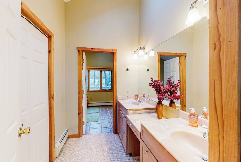 A bathroom with a double sink, a large mirror, and a door leading to another room.