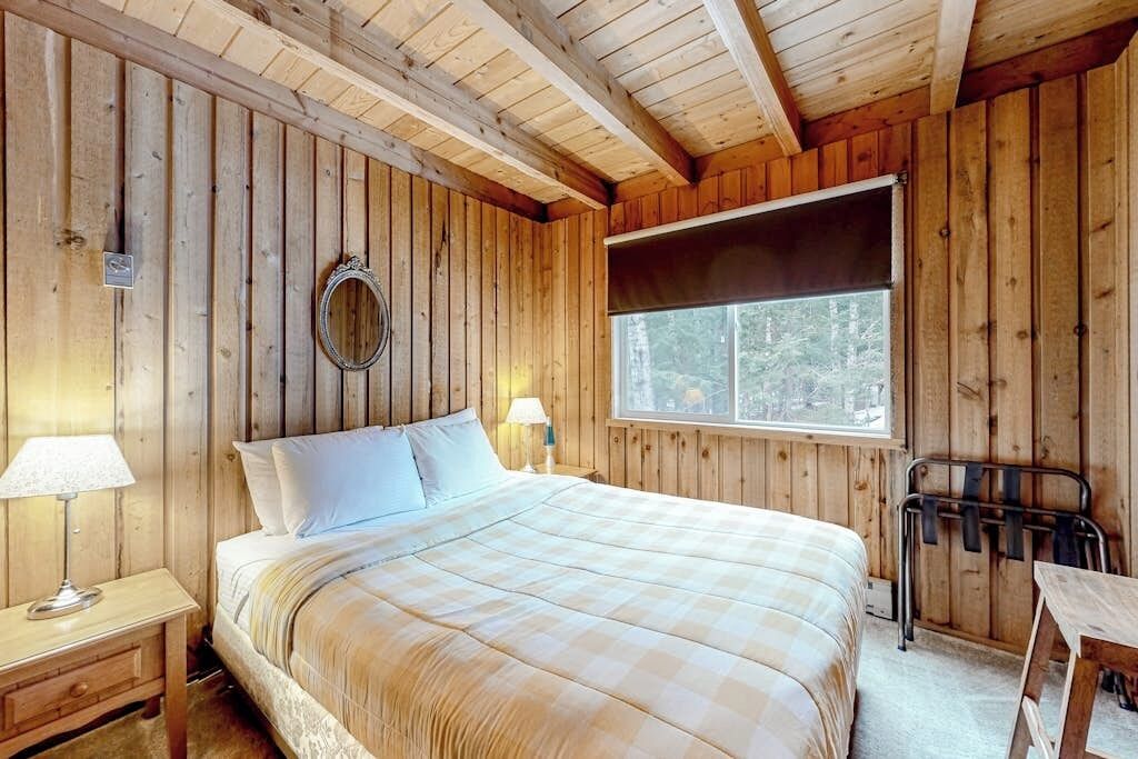 A wooden cabin room with a bed, a window, a mirror, and a table.