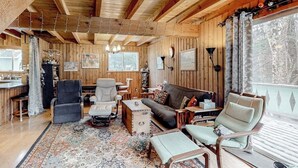 Ein Holzblockhaus-Interieur mit einer Couch, Sesseln, einem Couchtisch und einem Bücherregal.
